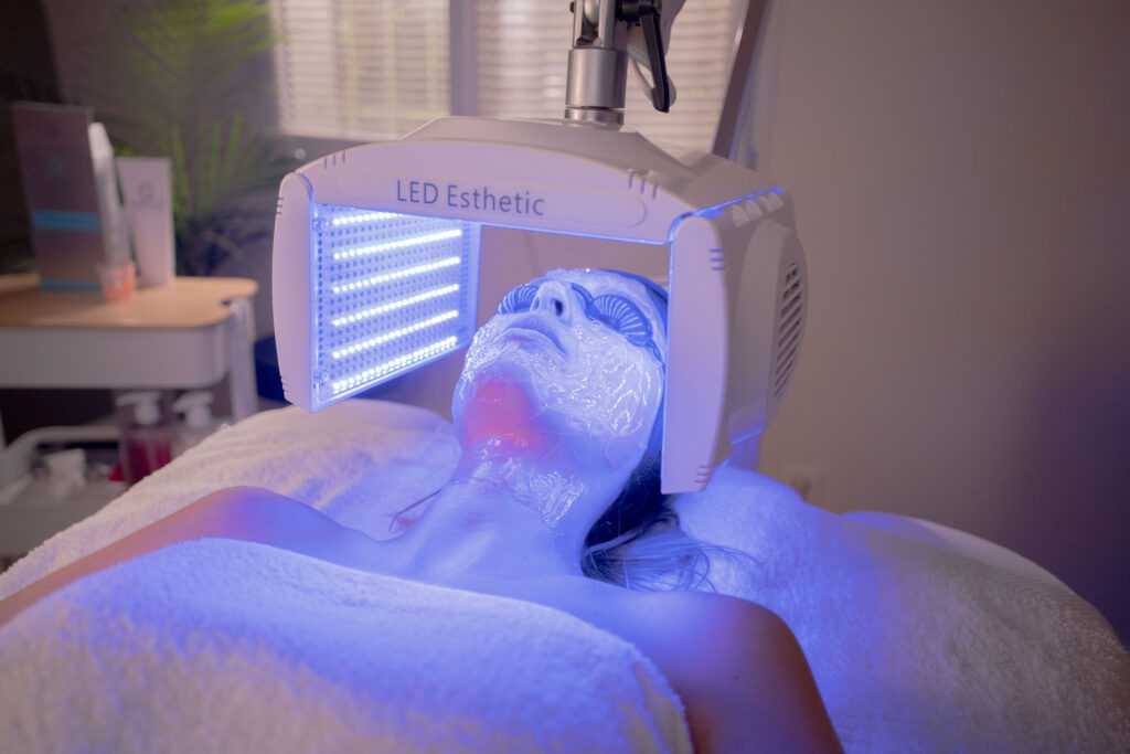 Séance de luminothérapie LED à lumière bleue sur le visage d'une cliente allongée, les yeux protégés